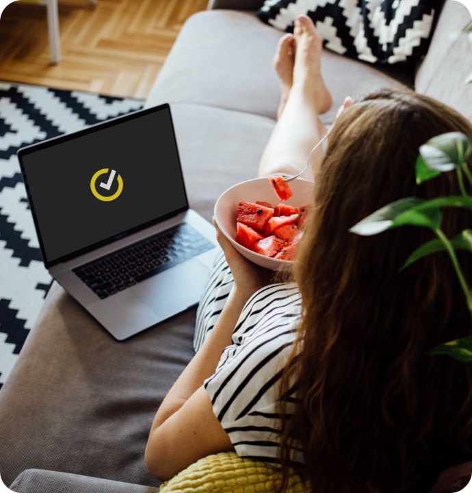 Dizüstü bilgisayarda Norton 360 AntiVirus Plus’ı kullanarak kanepede karpuz yiyen kadın